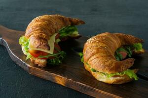 Croissant sandwiches with salted salmon on a desk, served with fresh salad leaves, arugula and vegetables over black background photo