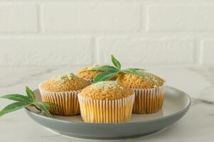 Healthy and tasty vegan and gluten free muffins in a row topped with hemp seeds on a marble table. Marijuana cupcake muffins with cannabis leaves photo