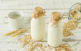 Oat milk in glass bottles and oatmeal in a cup on a wooden table. photo