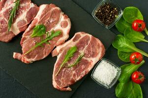 Fresh raw pork chop meat on a plack slate with rosemary and parsley and black pepper photo