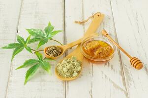 Honey dipper with Cannabis leaves, CBD Hemp honey, seeds and powder. Alternative medicine ingredients on wooden table photo