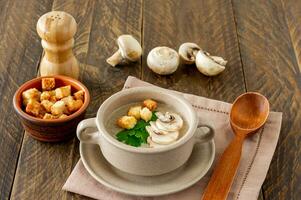 Mushroom cream soup with champignons, croutons and fresh herbs on rustic white wooden table photo