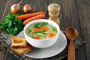 Fresh bouillon in a white bowl with finely chopped herbs with parsley and garlic on a wooden table. Hot soup made from chicken meat, carrots, onions, garlic, parsley and pepper. photo