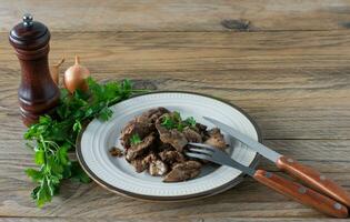 Cooked chicken liver with onion on a plate served on wooden desk. Rustic style photo