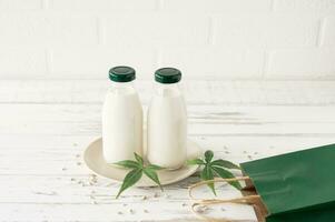 Bottles with Cannabis herbal vegan gluten and lactose free milk and cannabis leaves on wooden table photo