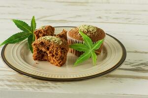 muffins veganos y sin gluten sanos y sabrosos en una fila cubiertos con semillas de cáñamo sobre una mesa de mármol. muffins de magdalenas de marihuana con hojas de cannabis foto