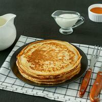 Stack of pancakes or crepes on a plate served with sour cream. Traditional food for the Russian pancake week. Wooden background photo