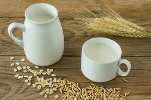 Oat milk in glass pitcher and oatmeal in a cup on a wooden table. photo