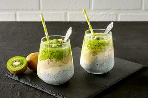 Chia seed pudding with kiwi, banana and mango. Health detox breakfast in glasses on black stone background photo