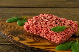 Raw minced beef meat on a wooden cutting board with vegetables and spices. Cooking and healthy eating concept. photo