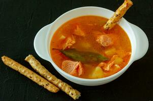 homemade soup with salmon with bread sticks on back concrete background photo