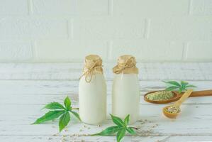Bottles with Cannabis herbal vegan gluten and lactose free milk and cannabis leaves on wooden table photo