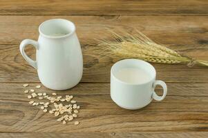 Oat milk in glass pitcher and oatmeal in a cup on a wooden table. photo