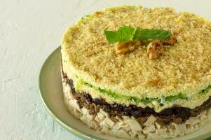 Layered salad with chicken, mushrooms, prunes, eggs, cucumbers and cheese served on a plate on white background photo