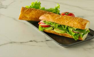 Sándwich vegano de baguette larga integral con lechuga, aguacate, tomate y queso. merienda saludable y comida para llevar foto