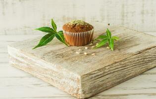 Healthy and tasty vegan and gluten free muffins topped with hemp seeds on a white plate on wooden table. Marijuana cupcake muffins with cannabis leaves photo