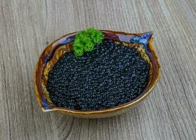 Black caviar in a bowl on wooden background photo