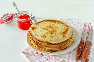 Traditional Russian Crepes Blini stacked in a plate with red caviar on wooden background. Maslenitsa traditional Russian festival meal. Russian food, russian kitchen. Close up. photo