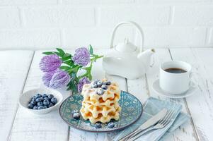 Homemade vanilla waffles with sugar powder and fersh blueberries on a plate, perfect family breakfast photo