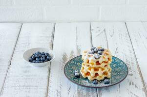 Square belgian waffles with blueberries and icing sugar on a blue plate. Tasty sweet sugary waffles photo