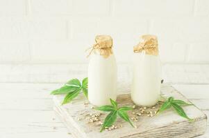 Bottles with Cannabis herbal vegan gluten and lactose free milk and cannabis leaves on wooden table photo