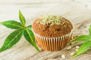 Healthy and tasty vegan and gluten free muffins in a row topped with hemp seeds on a marble table. Marijuana cupcake muffins with cannabis leaves photo