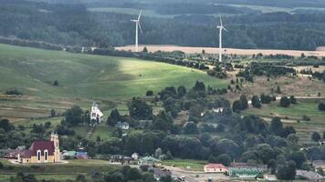 antenne panoramisch visie van groen dorp met windmolens Aan heuvel video