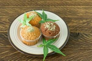 Healthy and tasty vegan and gluten free muffins topped with hemp seeds on a white plate on wooden table. Marijuana cupcake muffins with cannabis leaves photo