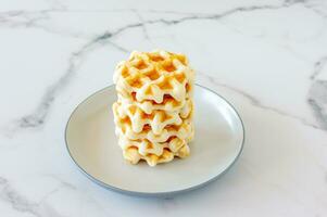 Belgian waffles stacked on white plate on marble table. photo