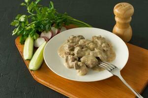 Cooked chicken liver with onion and sour cream sauce on a plate served on wooden desk. Rustic style photo