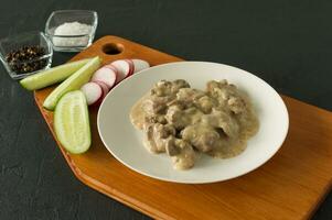 Cooked chicken liver with onion and sour cream sauce on a plate served on wooden desk. Rustic style photo