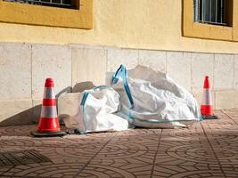 large bags of construction debris lie next to the wall of the building and are fenced with restrictive cones photo