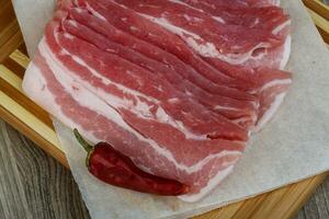 Raw bacon on wooden board and wooden background photo