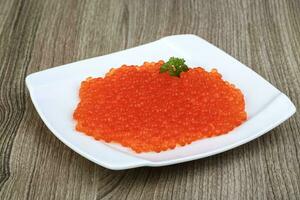 Red caviar on the plate and wooden background photo