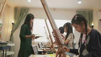 un grupo de niños multirraciales que aprenden con una mujer asiática enseña pintura acrílica en color sobre lienzo en el aula de arte, aprendiendo creativamente con habilidad en la educación de estudio de la escuela primaria. video