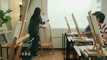 una maestra asiática enseña y demuestra a los niños sobre pintura acrílica en color sobre lienzo en el aula de arte, aprendiendo creativamente con habilidad en la educación de estudio de la escuela primaria. video