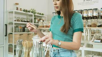 A young Caucasian female customer chose usable and recycled straws, shopping for organic products in refill store, zero-waste grocery, and plastic-free, environment-friendly, sustainable lifestyles.