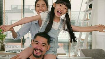 Asian Thai family together, dad plays and teases with daughter and mum by carrying and holding girl on shoulders in home living room, happy leisure times, lovely weekend, wellbeing domestic lifestyle. video