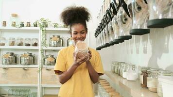la joven afroamericana está eligiendo y comprando productos orgánicos en una tienda de recarga, un frasco de vidrio reutilizable, una tienda de comestibles sin desperdicio y estilos de vida sostenibles, ecológicos y libres de plástico. video