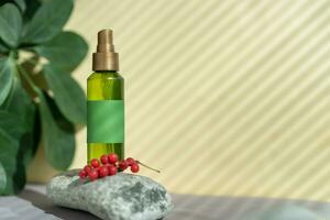 A bottle of green color with a spray bottle lies on the stones, next to the green leaves and berries of schisandra chinensis photo