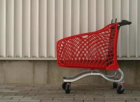 Empty red shopping on industrial wall background. Shop trolley at supermarket. Sale, discount, shopaholism, black friday, economy concept. Consumer society trend. Online Shopping Concept. photo