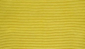 Texture of smooth knitted yellow sweater with pattern. Top view, close-up. Handmade knitting wool or cotton fabric texture. Background of knitting patterns. photo