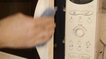 um homem limpa a extremidade da porta do micro-ondas com um pano úmido.limpando o forno de micro-ondas sujo video