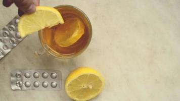 Man throws a slice of lemon into a cup of lemon tea on background of lemon and pills.Autumn decease. video