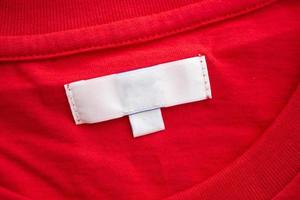 White blank clothing tag label on new red cotton shirt fabric texture background photo