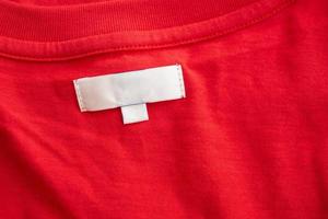 White blank clothing tag label on new red cotton shirt fabric texture background photo