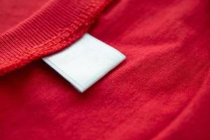 White blank clothing tag label on new red cotton shirt fabric texture background photo