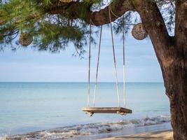 columpio de madera colgado en el árbol en el fondo es un mar azul. foto