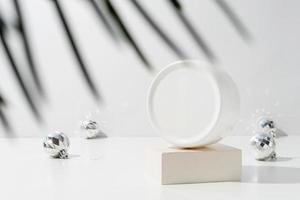 A minimalistic scene of plastic cream box on podium with christmas decorative balls and pine tree on light background photo