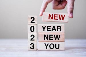 hand holding wooden block with text 2023 NEW YEAR NEW YOU on table background. Resolution, strategy, goal, business and holiday concepts photo